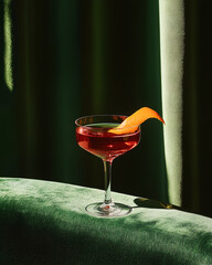Red cocktail in elegant coupe glass with orange peel garnish on green velvet