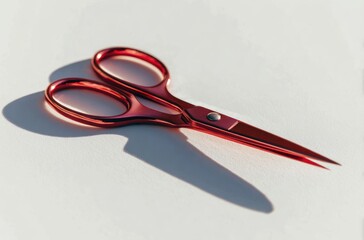 Gleaming reddish-pink scissors cast sharp shadow on a clean white surface, highlighted by bright sunlight