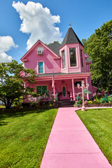 A really pink house with a pink sidewalk and a pink porch on a perfect summer day
