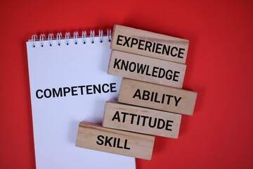 Notebook and wooden blocks displaying competence and essential qualities like experience, knowledge, and skill against a red background. Visualizing development and personal or professional growth.