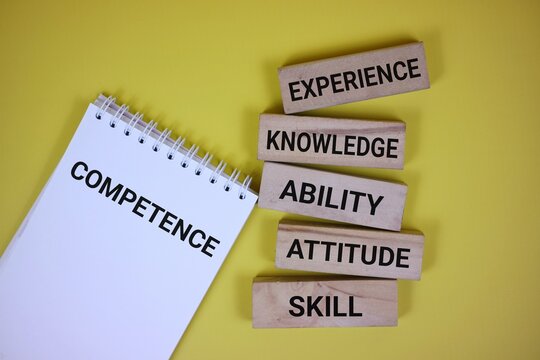 Notebook and wooden blocks displaying competence and essential qualities like experience, knowledge, and skill against a yellow background. Visualizing development and personal or professional growth.