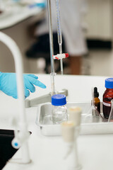 Close-up of a gloved hand in a laboratory using burette and beakers during chemical experiment, research, or educational demonstration