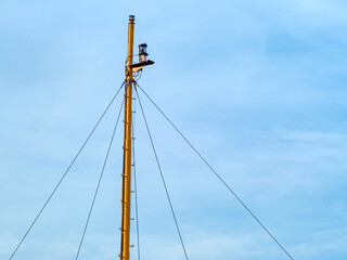 Fototapeta premium A yellow communications mast stands tall against a clear blue sky fitted with multiple security cameras and antennas for surveillance and observation