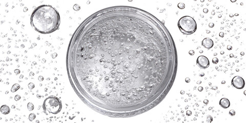 Clear, circular container filled with a translucent liquid, featuring numerous small bubbles. Surrounding the container are many small, speckled particles