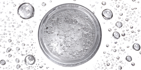 Clear, circular container filled with a translucent liquid, featuring numerous small bubbles. Surrounding the container are many small, speckled particles