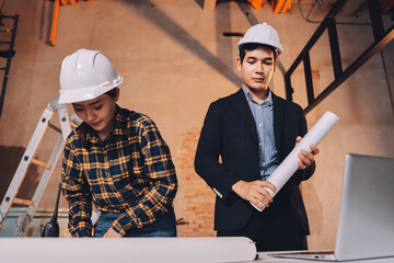 Construction manager and engineer dressed in orange work vests and hard helmets explore construction documentation on the building site near the steel frames
