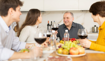Senior man at kitchen table with wife, grown son and daughter, enjoying conversation at festive table with wine and light snacks