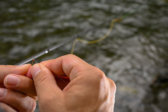 Angler preparing fishing rod, tying line to hook, with river in background