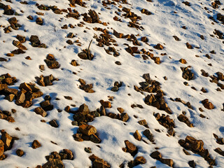 Sunlight casts long blue shadows across a snow covered rocky field creating a beautiful high contrast natural texture of light and shade during a cold winter day