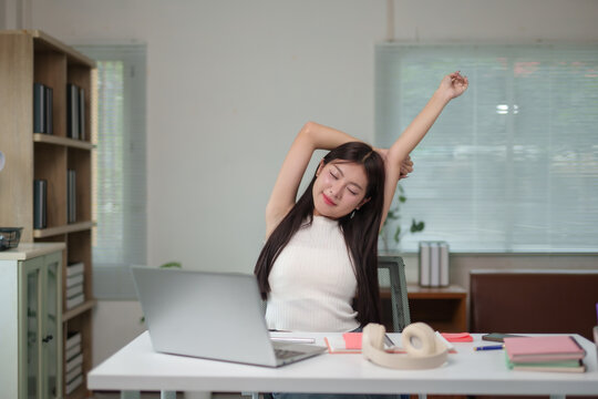 Asian woman stretching arms while working from home, enjoying break time after long work on laptop computer - Powered by Adobe