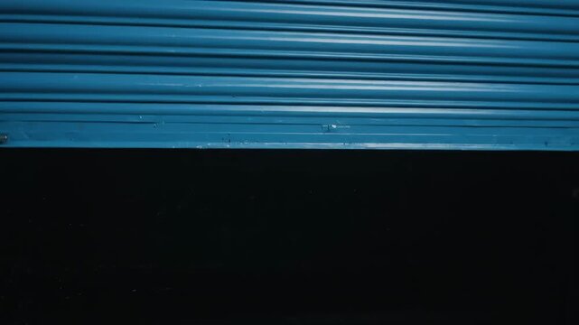Teal Blue Metal Rolling Shutter Door Partially Raised - A partially raised teal blue metal rolling shutter door is shown against a black background.