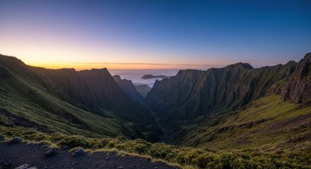 Fototapeta premium Lush green mountain valley at sunrise, with clouds visible between peaks