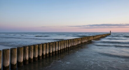 Obraz premium Wooden breakwater stretches into the sea during a soft sunset sky