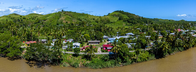 Panoramic aerial view of a traditional Fijian village with colorful houses nestled amongst palm...