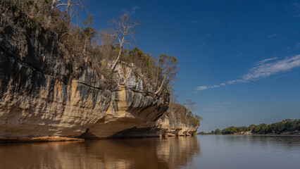 A calm red-brown African river. Trees grow on the steep limestone eroded shores. Blue sky, clouds....