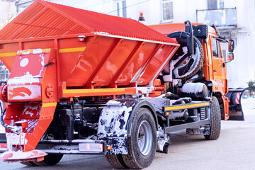 Orange snow removal machine standing on a snowy road during winter. Utility services vehicle for street cleaning and ice control.