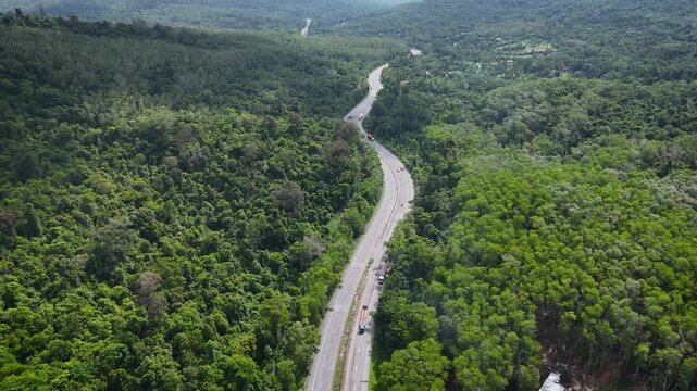 Drone footage of the aerial view of a winding road cutting through lush green forest. Scenic highway number 304 in Thailand links the Bangkok area to Nakhon Ratchasima in the northeastern region