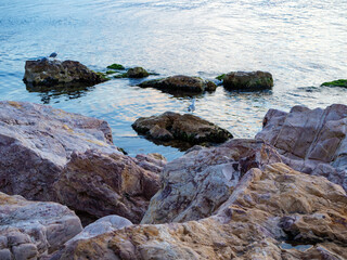 Large weathered rocks emerge from the tranquil clear sea water on a calm day creating a rugged and beautiful natural coastal landscape