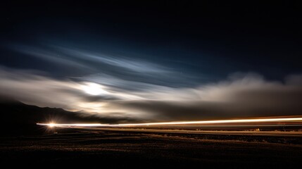 Night landscape with long exposure light trails under cloudy sky and moonlit clouds illuminating the distant hills