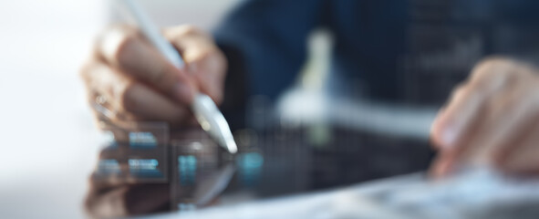 Hand holding a stylus pen over a dark surface in a blurred setting.