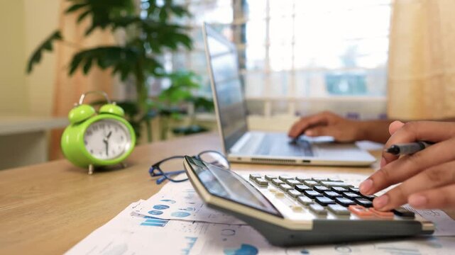 Business Analysis at Home Office Desk, Person using calculator and laptop at desk with charts and clock