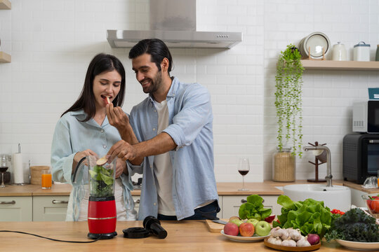 Couple preparing healthy smoothie in kitchen with blender, fresh fruits and vegetables for wellness lifestyle