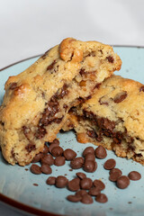 Galleta casera partida con chispas de chocolate derretido sobre plato azul, estilo artesanal y apetitoso ideal para repostería gourmet.