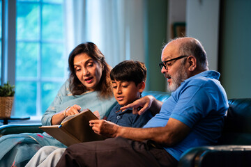 Reading Grandparents reading storybook with child while sitting on sofa at home indoors