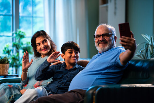 Indian grandparents with grandchild using smartphone for video call while sitting indoors - Powered by Adobe