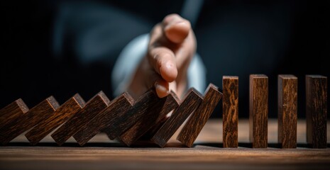 Man stops cascading wooden dominoes on a wood surface, preventing further topple