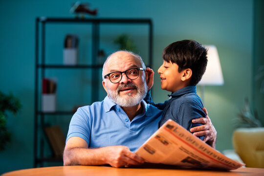 Indian boy shares gossip secretly with grandfather at home sitting at table