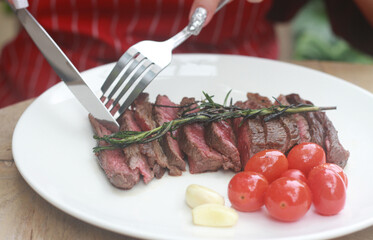 A steak on a white plate ready to eat, garnished with red tomatoes and rosemary for flavor.