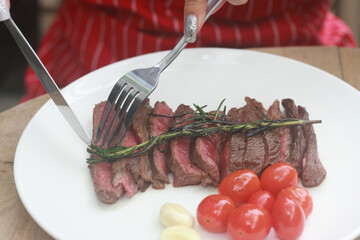 A steak on a white plate ready to eat, garnished with red tomatoes and rosemary for flavor.