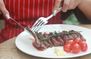 A steak on a white plate ready to eat, garnished with red tomatoes and rosemary for flavor.