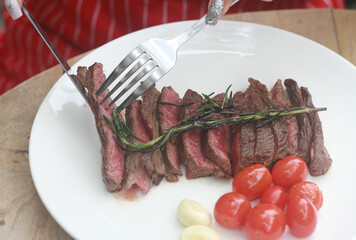 A steak on a white plate ready to eat, garnished with red tomatoes and rosemary for flavor.