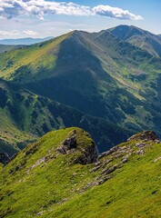 Fototapeta premium Scenic mountain ridge with green grassy slopes, rocky outcrops, and distant peaks under a blue sky. Natural alpine landscape ideal for hiking and nature lovers.