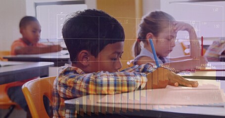 Writing focused boy working in notebook on orange chair in classroom, with pencils, chart overlays