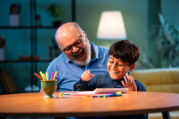 Indian grandfather helps boy with drawing and coloring while sitting at table