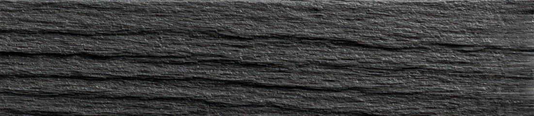 A dark gray, textured surface shows subtle horizontal striations and grain. The material appears rough, with varying shades of gray