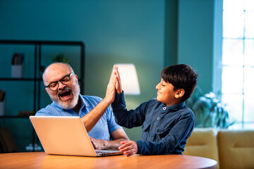 Indian boy teaches grandfather laptop usage at home, sharing family bonding