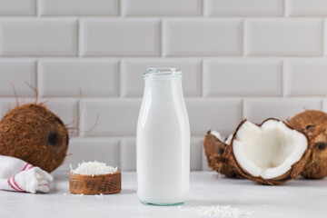 Fresh coconut milk in glass bottle with whole and halved coconuts. Vegan healthy milk