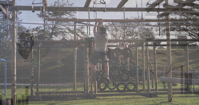 Climbing athletic male swinging on hanging rings in grassy park obstacle course, training partners
