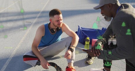 Resting mid adult male athlete sitting on outdoor track, with coach holding tablet and data icons