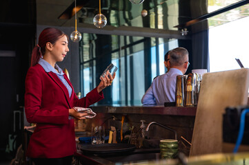 Asian bartender woman checking cocktail glass working behind counter bar
