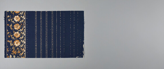 A refined blue fabric swatch with a rich gold floral border on one side, complemented by subtle vertical stripes of gold dots, elegantly presented on a sophisticated grey background.
