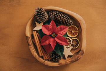 Overhead shot of wooden bowl filled with pine cones poinsettia cinnamon sticks and dried orange slices