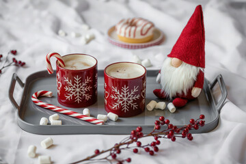 Festive tray with hot chocolate, candy canes, donut, gnome, and marshmallows on white bedding