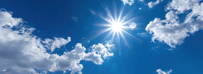 Radiant sunlight bursts in a clear, bright blue sky with fluffy, white clouds scattered across the vast expanse