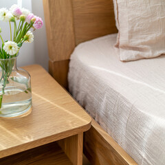 Wooden bedside table with glass vase and flowers in soft daylight
