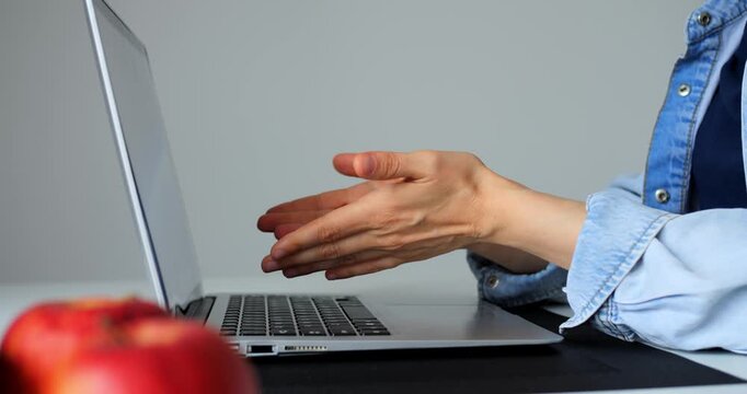 Female professional typing on laptop keyboard, warming hands during remote work session, red apple nearby on minimalist workspace with natural lighting